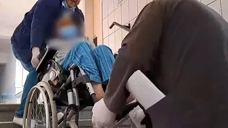 VIDEO | Scene revoltătoare într-un spital din Reșița! Pacienții imobilizați sunt cărați pe brațe de infirmieri pentru că în clădire nu există lift
