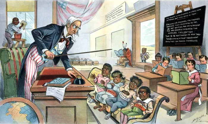 Caricatură din 1899 care îl prezintă pe Unchiul Sam ca învățător, stând în spatele unui birou în fața noilor săi elevi, etichetați „Cuba, Porto Rico, Hawaii și Filipine”; aceștia nu par fericiți să fie acolo. În spatele clasei, se află elevi conștincioși care citesc cărți etichetate „California”, „Texas”, „New Mexico”, „Arizona” și „Alaska”. În partea stângă, un băiat afro-american curăță geamurile, în fundal, un băiat nativ stă singur, citind o carte întoarsă pe dos etichetată „ABC”, iar un băiat chinez stă chiar în afara ușii. Pe biroul lui Unchiul Sam se află o carte intitulată „Primele lecții de autoguvernare ale SUA”. Sursa Foto: Profimedia 