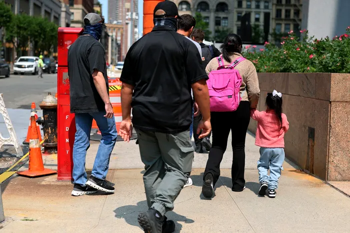 O femeie migrantă și copilul ei sunt escortați de agenții federali după ce au ieșit dintr-un birou al Programului de Supraveghere Intensivă din New York FOTO: Profimedia