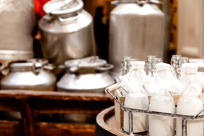 Glass bottles with fresh natural milk, aluminum cans on hay on dairy farm. Healthy farm products