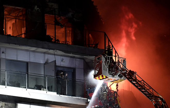Two residents stand on a balcony, prior to being rescued, as firefighters battle a huge fire raging through a multistorey residential block in Valencia on February 22, 2024. Spanish firefighters were battling a huge fire raging through a multistorey residential block in the eastern port city of Valencia today, the emergency services said. Flames and vast clouds of black smoke engulfed the building, with 22 teams of firefighters battling high winds to tackle the blaze, the 112 emergency services said. In a post on X, formerly Twitter, the emergency services said seven people had been lightly injured: a minor, three adults and three firefighters, most of them suffering from smoke inhalation.,Image: 849553041, License: Rights-managed, Restrictions: ALTERNATIVE CROP, Model Release: no
